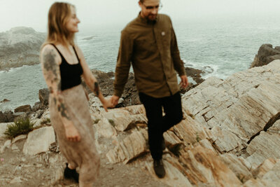 Couple holding hands and walking on rocky shoreline
