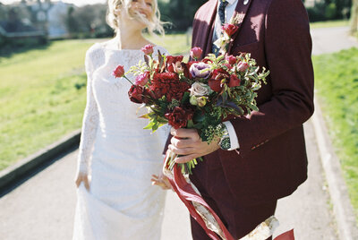 close up bride and groom walking and groom holding red bold bouquet