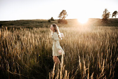 carefree senior photo of girl spinning in green field at sunset