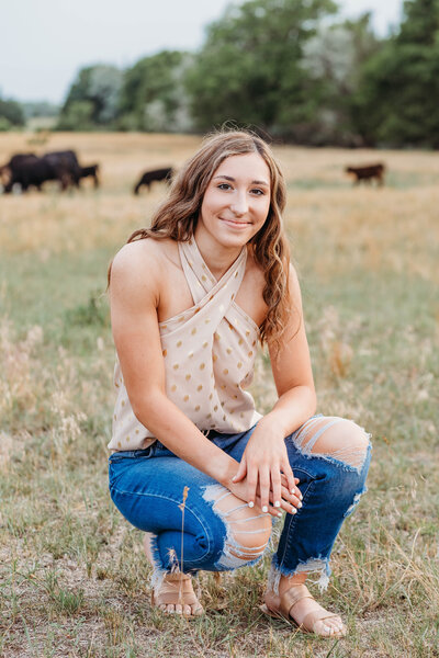 high school senior in a field with cows behind her