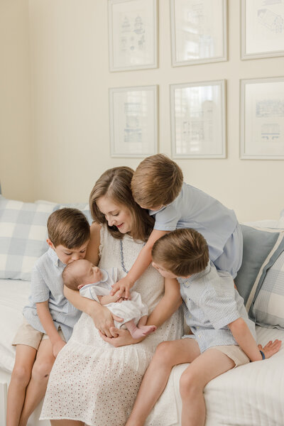 Mother holding newborn with her three sons looking down at the baby. -Newborn Photographer Greenville