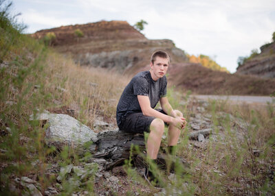 high school senior boy sitting on large rock in outdoor location
