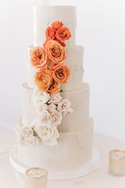 White tiered wedding cake with white and orange roses cascading down one side
