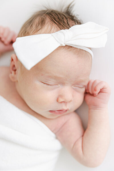 Sleeping newborn baby girl wears white bow during newborn portrait session