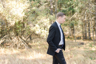 groom in field standing with his hands in his pocket and looking at the ground