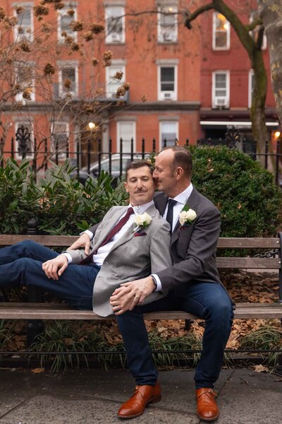 Two men sitting on a park bench while leaning up against each other.