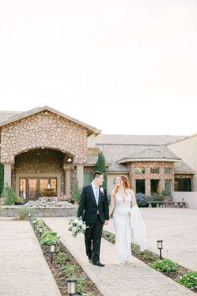 The bride embraces the groom, who stands with his back against the backdrop of roads and the stunning Superstition Manor mountains, capturing a moment of love against a scenic setting