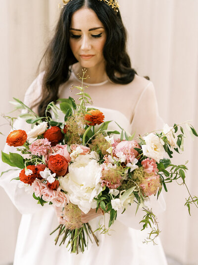 A midsummer nights dream bridal bouquet filled with ranunculus, peonies, garden roses, sweet pea and jasmine vine floral hues of red, dusty pink, taupe, and green. Designed by Rosemary and Finch in Nashville, TN.