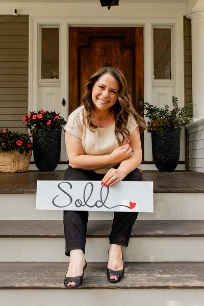 Realtor sitting on porch steps holding sign that reads 'sold' - link to branding photography