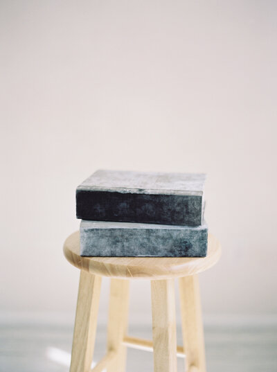 photo of two fine art newborn albums stacked on a wooden stool, made by madison wi photographer Talia Laird Photography