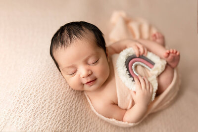 Newborn girl wrapped in Blue with soft rainbow adornment.