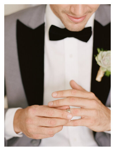Groom in grey tux putting on wedding ring