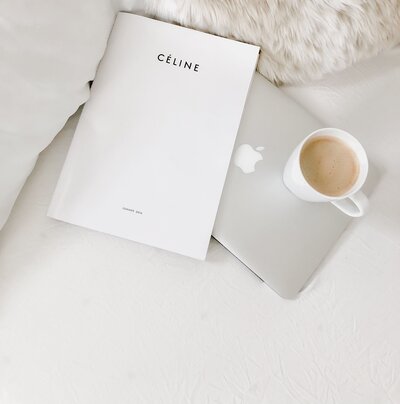 A laptop, coffee cup, and magazine on a bed.