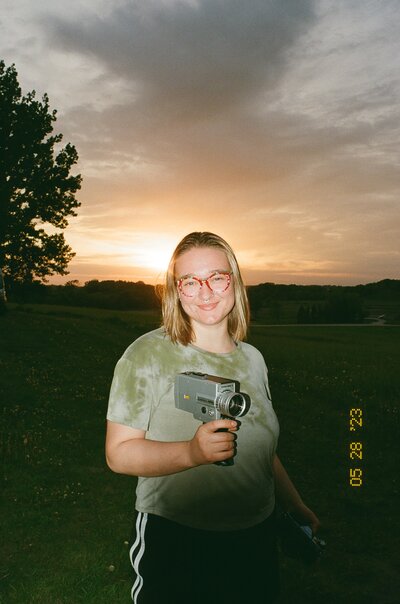 Brianna Kirk on 35mm film headshot against a sunset holding a vintage film super 8 camera