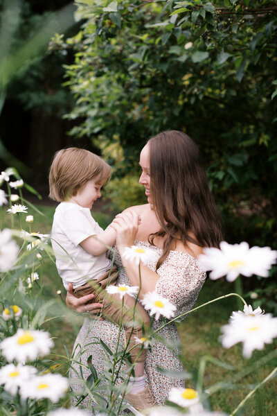 mom holds child on her hip surrounded by white summer flowers