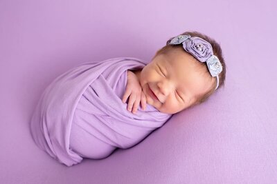 A newborn baby wrapped in a purple blanket.
