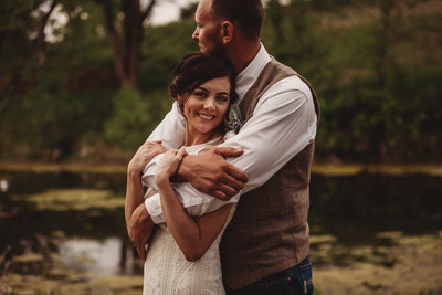 groom wraps around his bride in front of a pond in Kansas after their barn wedding ceremony | Native Roaming