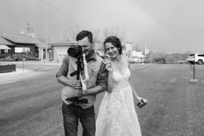 Groom holding camera while bride poses next to him