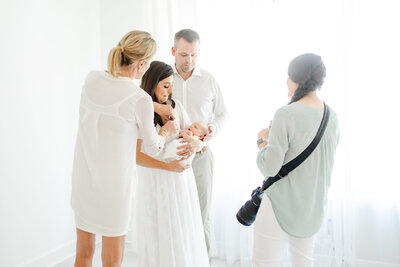 photographer and assistant help position a mother and father while holding their newborn baby during in-studio portrait session