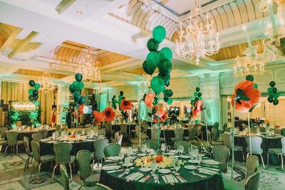Reception setup with green balloon centerpieces and bold red floral arrangements.
