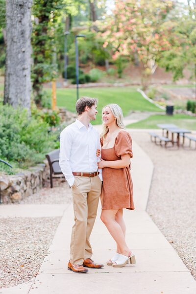 Engaged couple pose among flowers in brown and white outfits in a park in Arkansas.