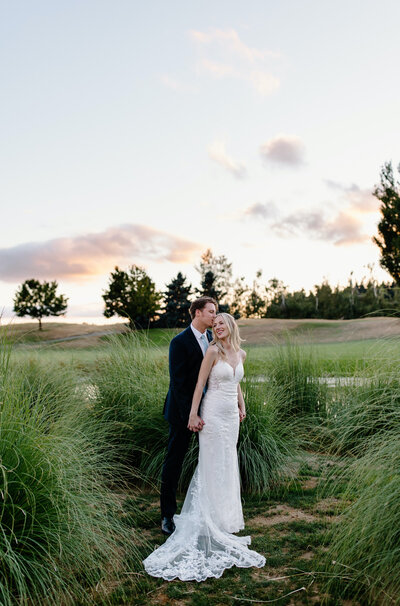 bride and groom in tall grass at sunset