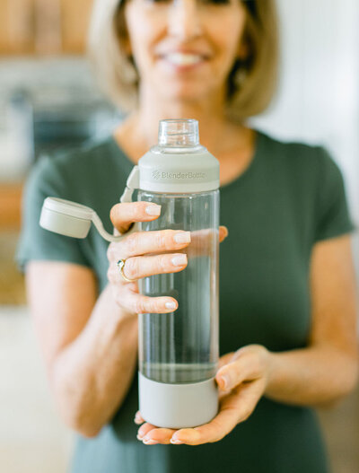 A smiling woman presenting a clear BlenderBottle, showcasing hydration or health routine