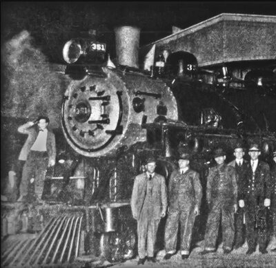 Several workers or owners stand in front of an engine in a vintage black and white photo at Union Station.