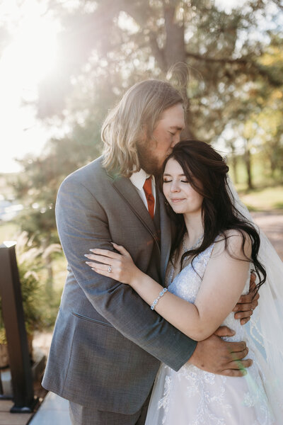 Bride and groom embracing in their first kiss while the bride raises the bouquet.