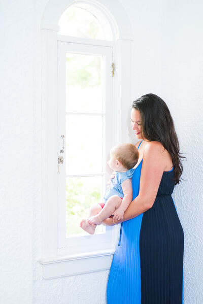 Mom and baby looking out the window in home christmas in miami lifestyle photo session by miami Christmas mini session photographer msp photography David and Meivys Suarez