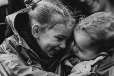 Brother and sister hugging and laughing in black and white image