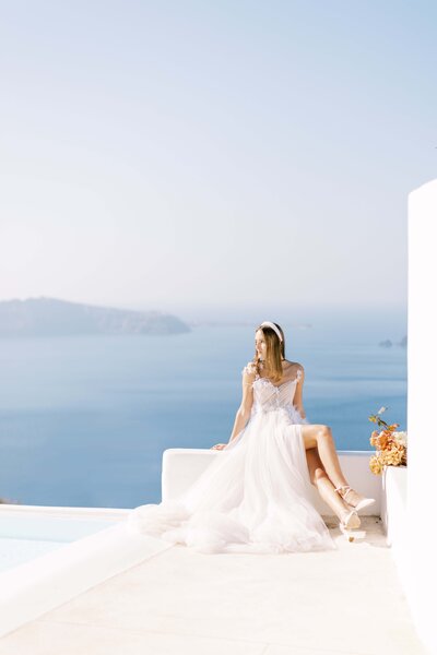 bridal portrait bride sitting in white gown with white headpiece overlooking santorini, santorini wedding photographer, greece wedding photographer, europe wedding photographer, destination wedding photographer