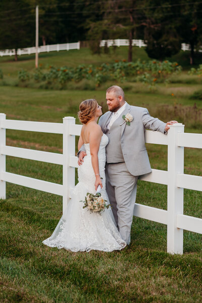 photo of bride and groom  hugging beside a white fence