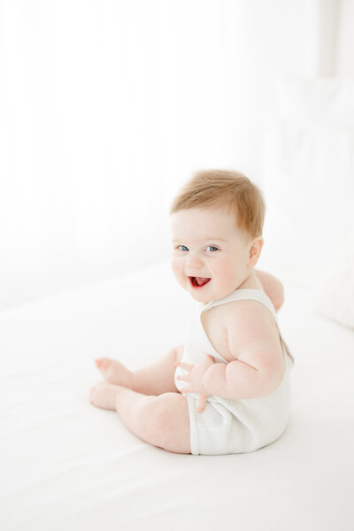 6 month old baby boy smiles and sits in cream overalls