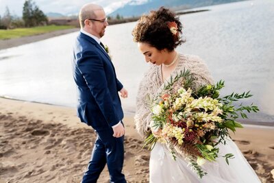 a bride in a shaggy sweater with a presentation bouquet walks along columbia river