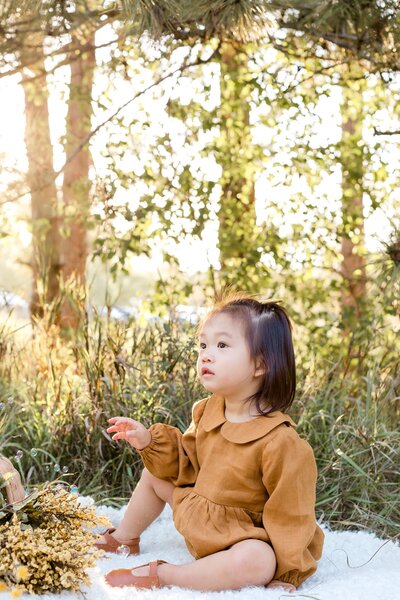 Infant sits on a blanket  in tall grass at sunset.