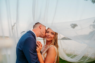 photo of a bride and groom with her veil flowing in the wind in front of a barn