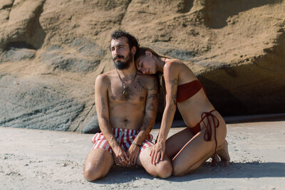 Tattooed couple wearing red and Candy stripe swimsuits pose on the beach near Sayulita with Mexico wedding photographer J.J. Au'Clair