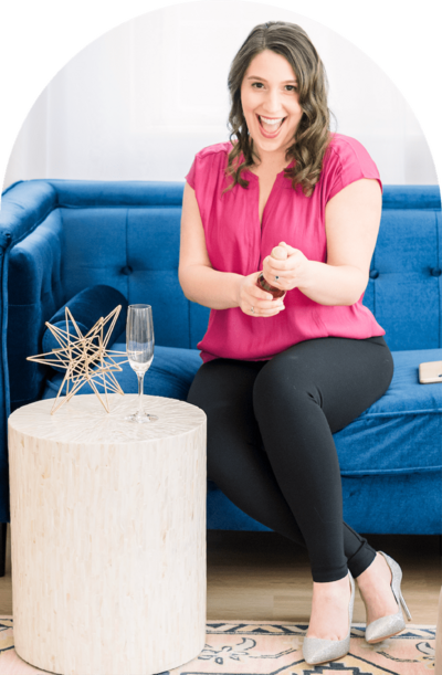 Isabel sitting on a blue couch popping a bottle of champagne in celebration of a client website launch.
