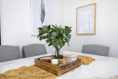 Bright sunroom with large windows, wicker dining chairs, and a timber table overlooking a leafy backyard.
