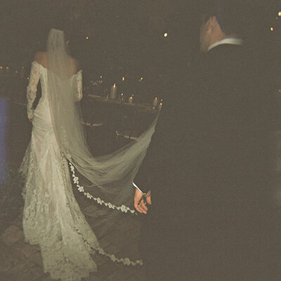 Film photo of bride walking away from camera while groom holds the end of her veil