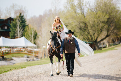 bride riding horse to wedding reception with dad pulling her there