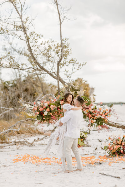 Bride and groom embrace with elaborate bouquet on the beach during their elopement
