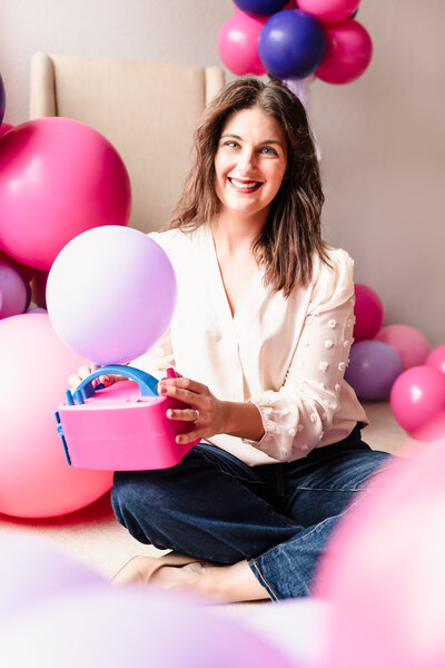 brand photo of a business owner among balloons, holding a machine to inflate balloons