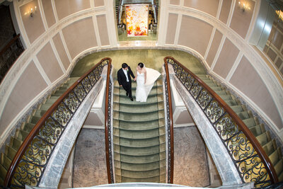 Bride and groom are walking down on a elegant indoor stairs.
