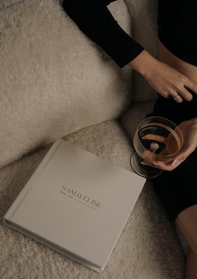 Wedding album on couch with a woman sitting next to it with mix drink in hand- Romero Album Design
