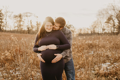 pregnant couple smiling together in a field