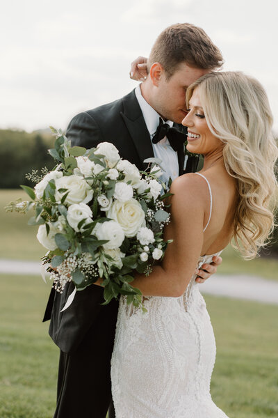 Bride holding large bouquet snuggled up with her husband on their wedding day