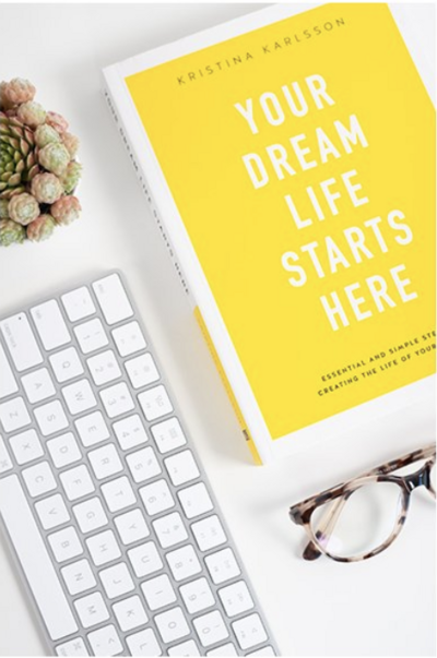 Yellow book that says "Your Dream Life Starts Here" on desktop next to plant and keyboard
