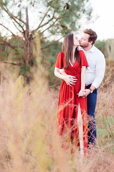 Couple kissing in front of trees and tall grass